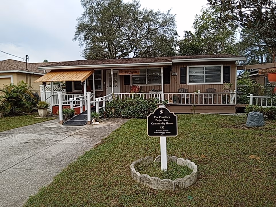 Single-story house with front porch, sign, and manicured lawn in a residential neighborhood.