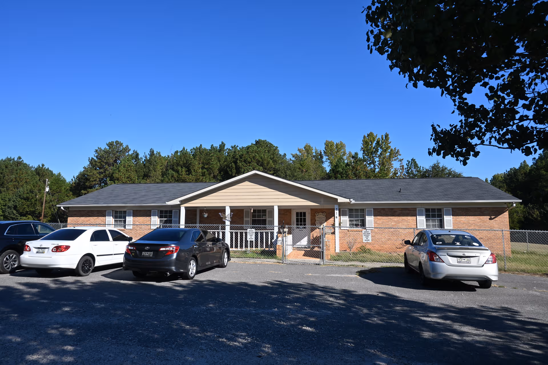 Brick single-story residential care facility with front entrance, parking, and chain-link fence.