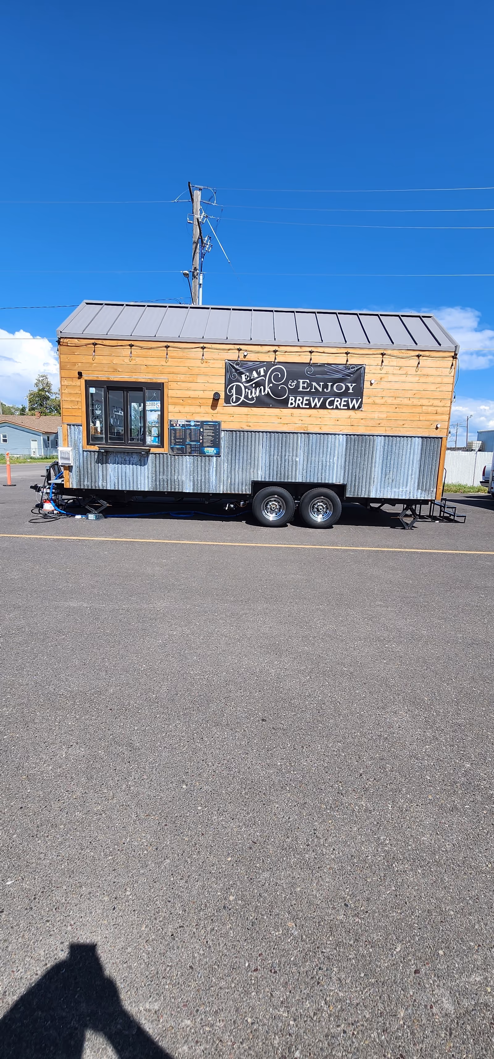 Wooden trailer on a paved lot with 'Eat Drink Enjoy Brew Crew' sign.