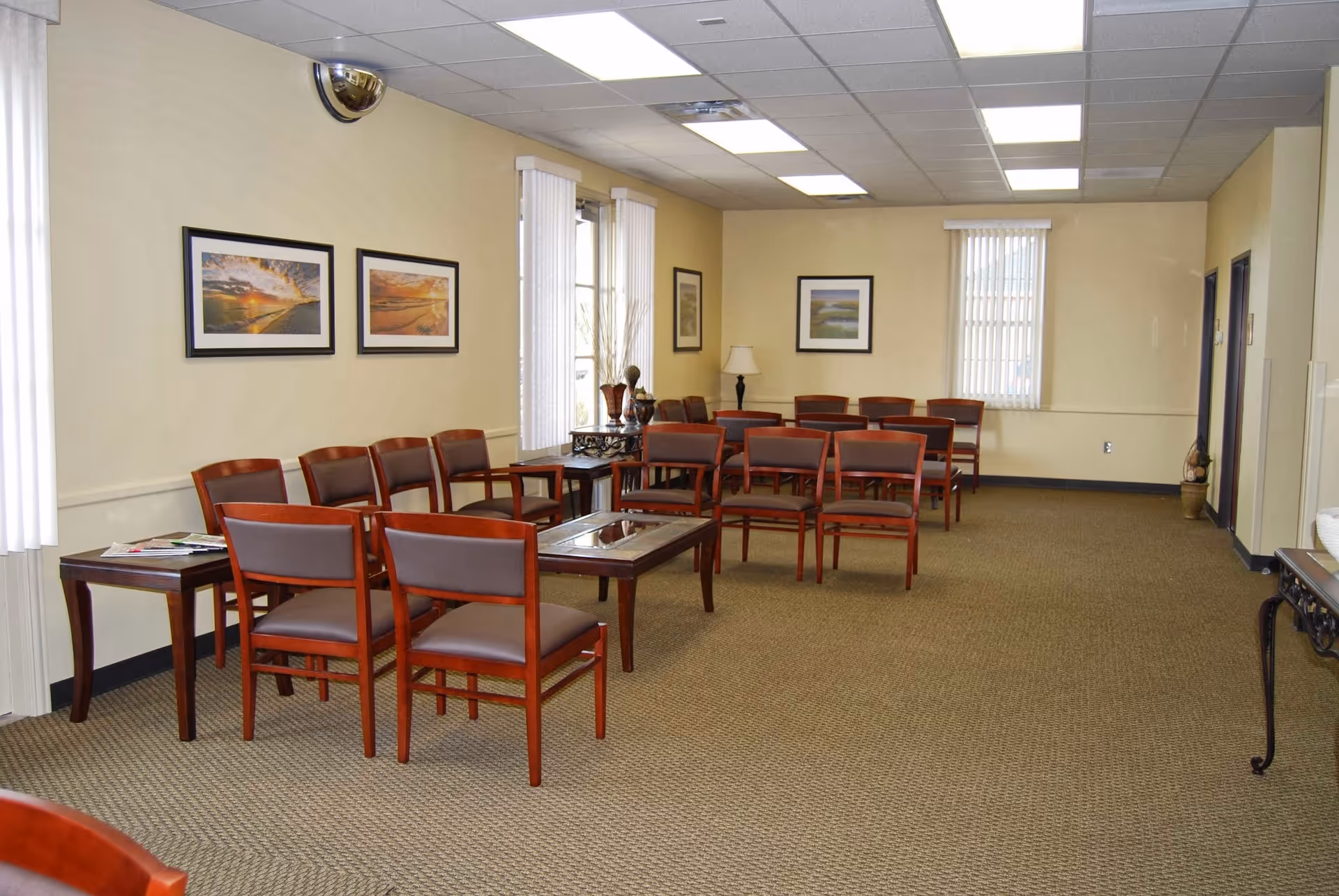 Spacious waiting area with rows of red-brown chairs, framed wall art, and windows.