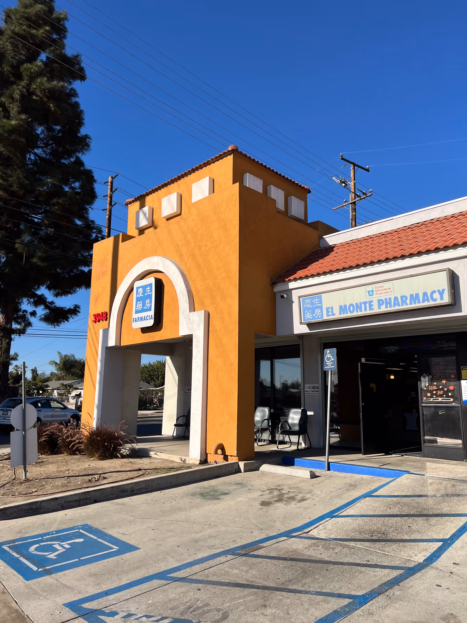 Orange stucco building with arched entry and El Monte Pharmacy sign near handicap parking.
