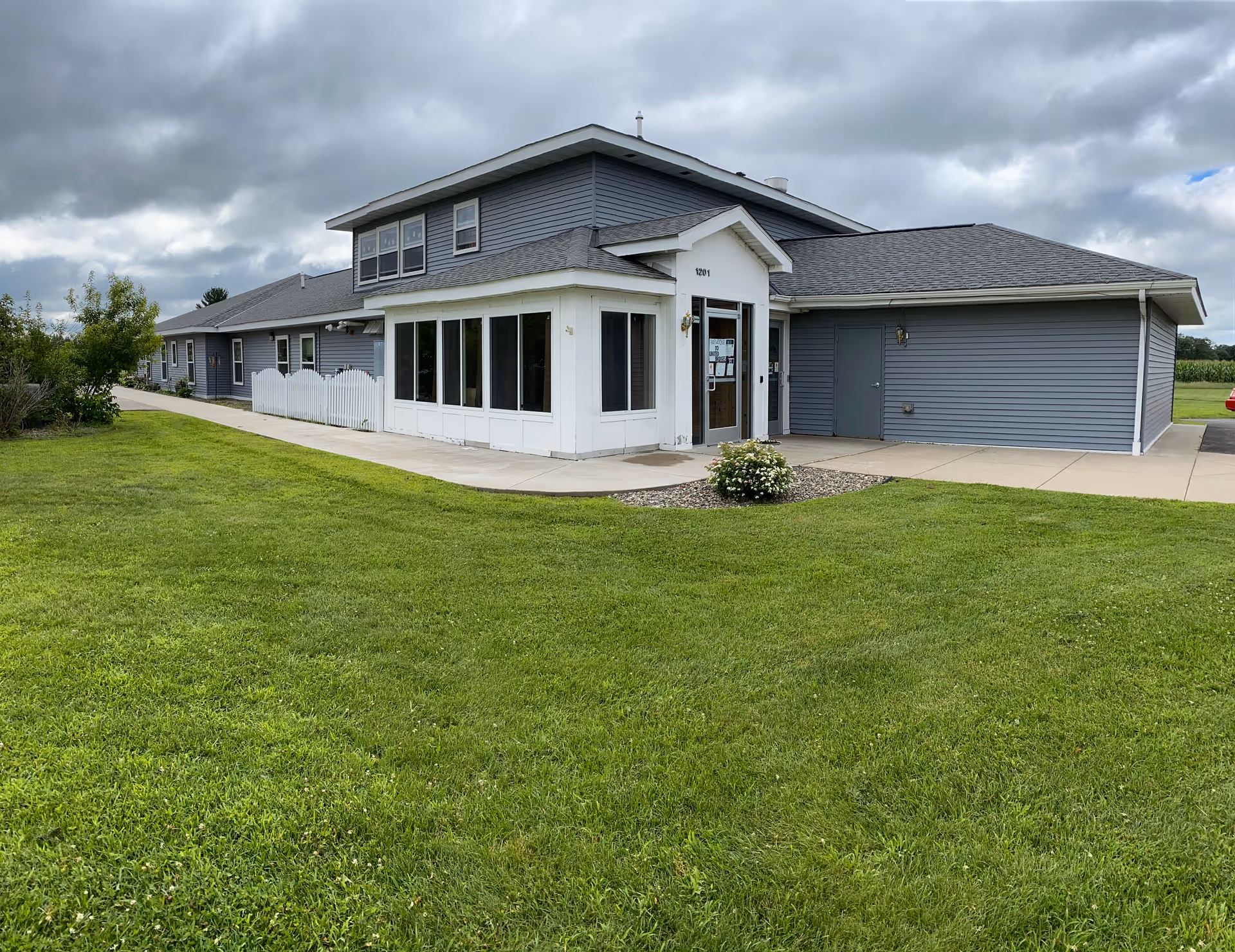 Single-story blue-gray senior living facility with white trim and a glass-front entrance.