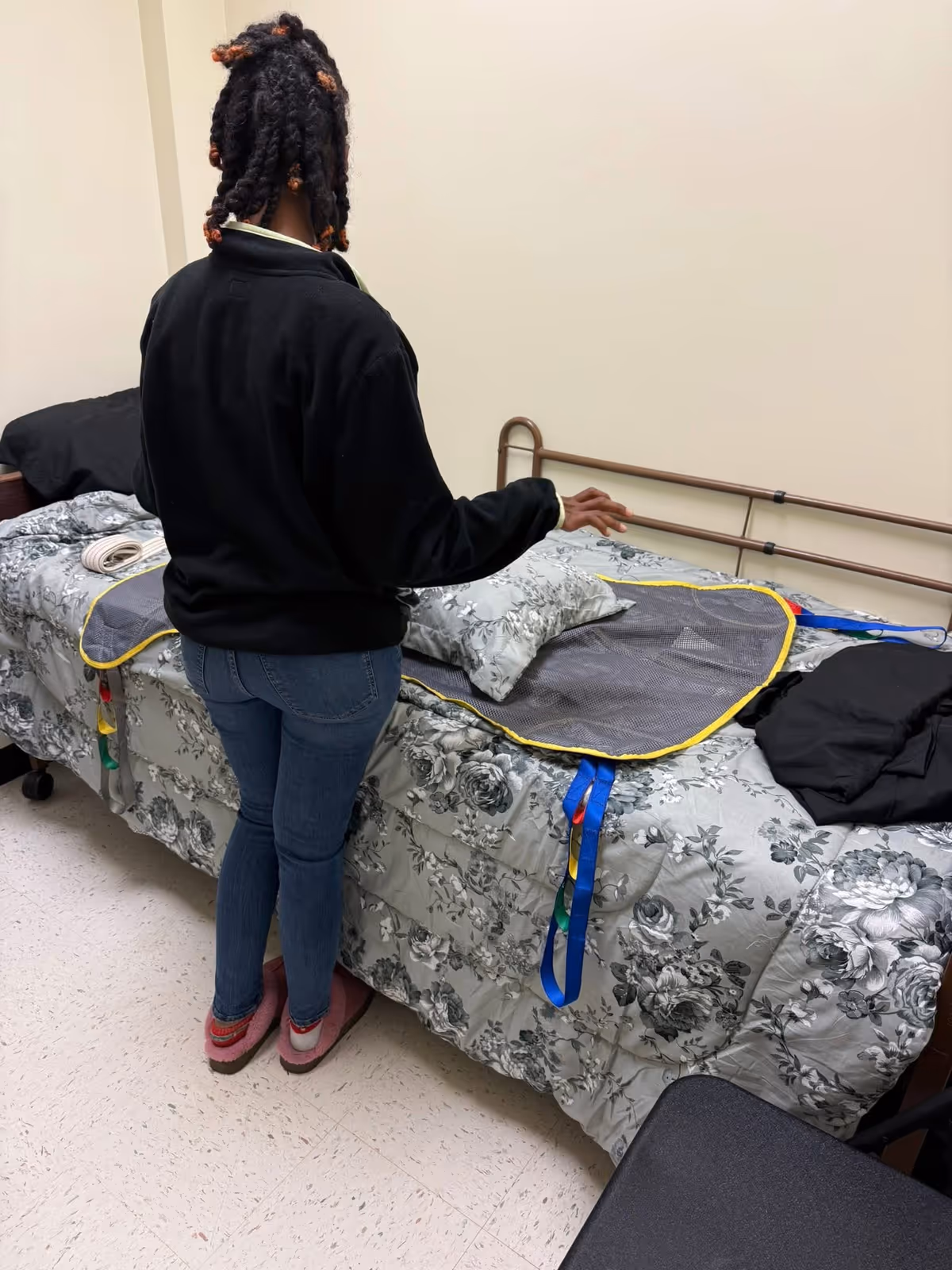 A person stands beside a floral bed in a facility bedroom.