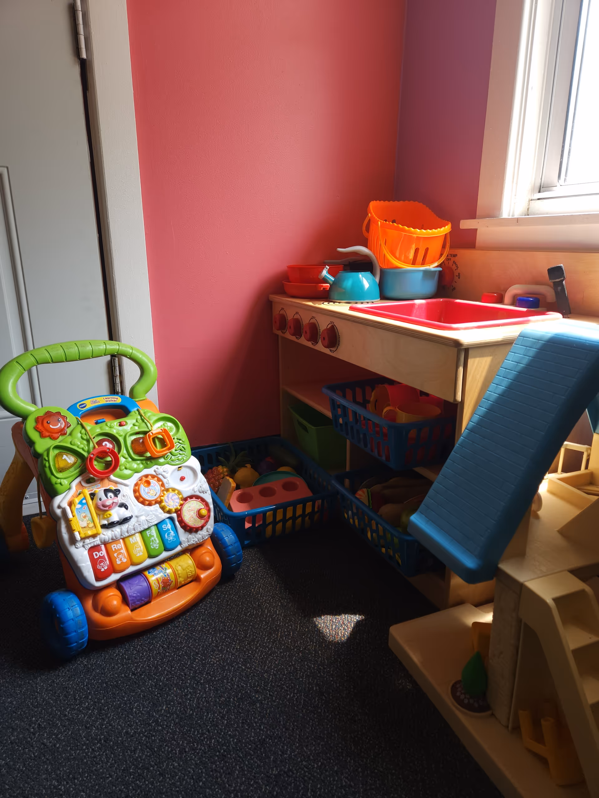 Colorful children's play kitchen and toys in a sunny corner of a bright interior.