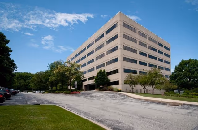 A large beige multi-story building with a curved driveway and surrounding trees.