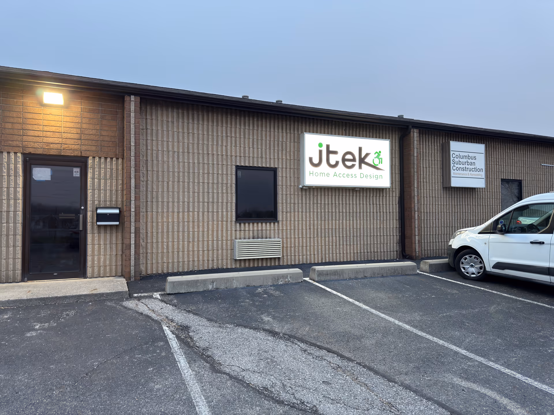 Exterior view of brick building with JTEK Home Access Design sign and parked van.