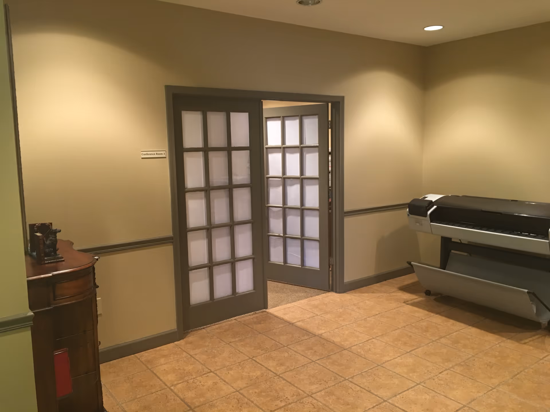 Interior hallway with French doors, a sign, printer, and wooden cabinet.