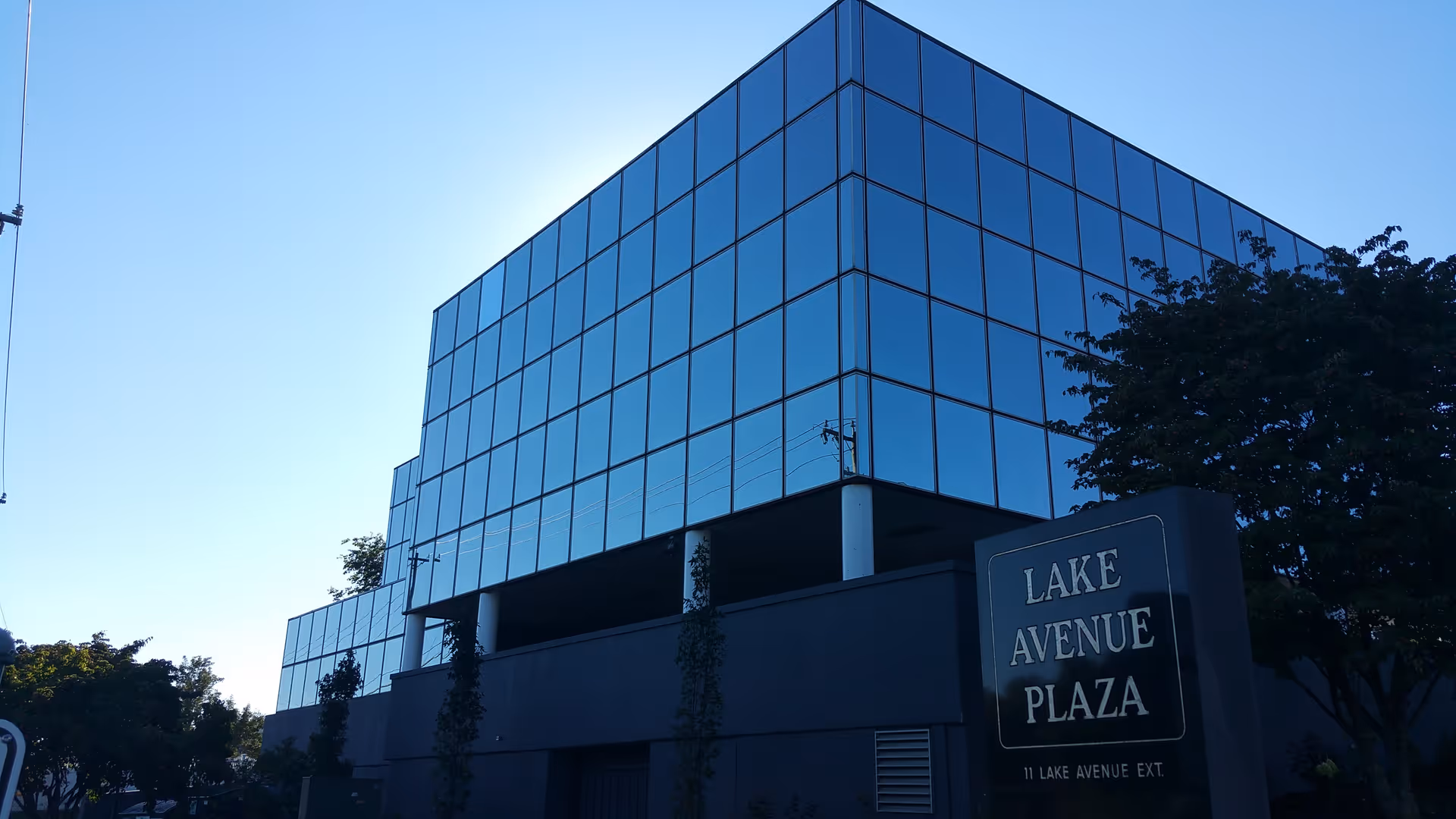 Modern glass-front building with Lake Avenue Plaza sign under a clear blue sky.
