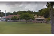 Exterior view of Ridgeland Nursing Center with trees, grassy lawn, and a fence.