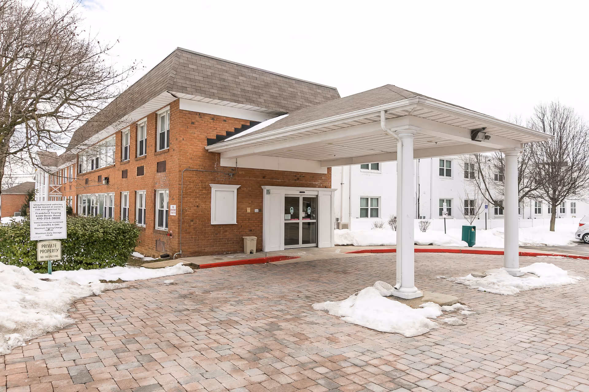 Brick nursing home with a covered entrance, snow on the ground, and leafless trees.