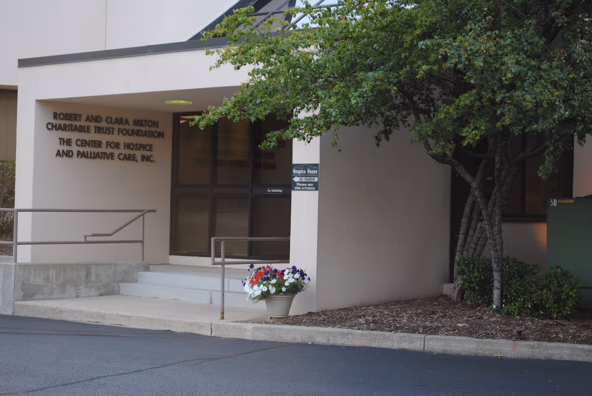 Exterior entrance of Center for Hospice Care with steps, railing, and potted flowers.