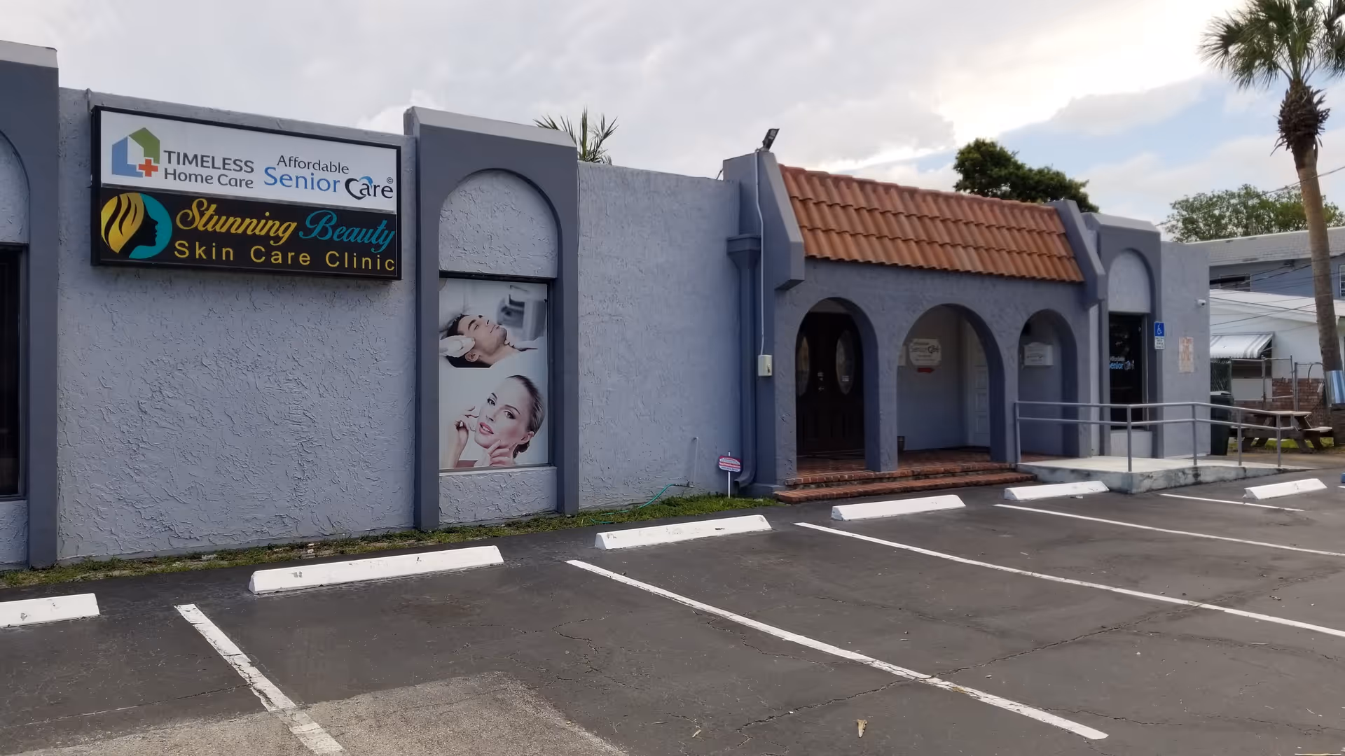Blue-gray storefront building with arched entry, signage, and parking lot.