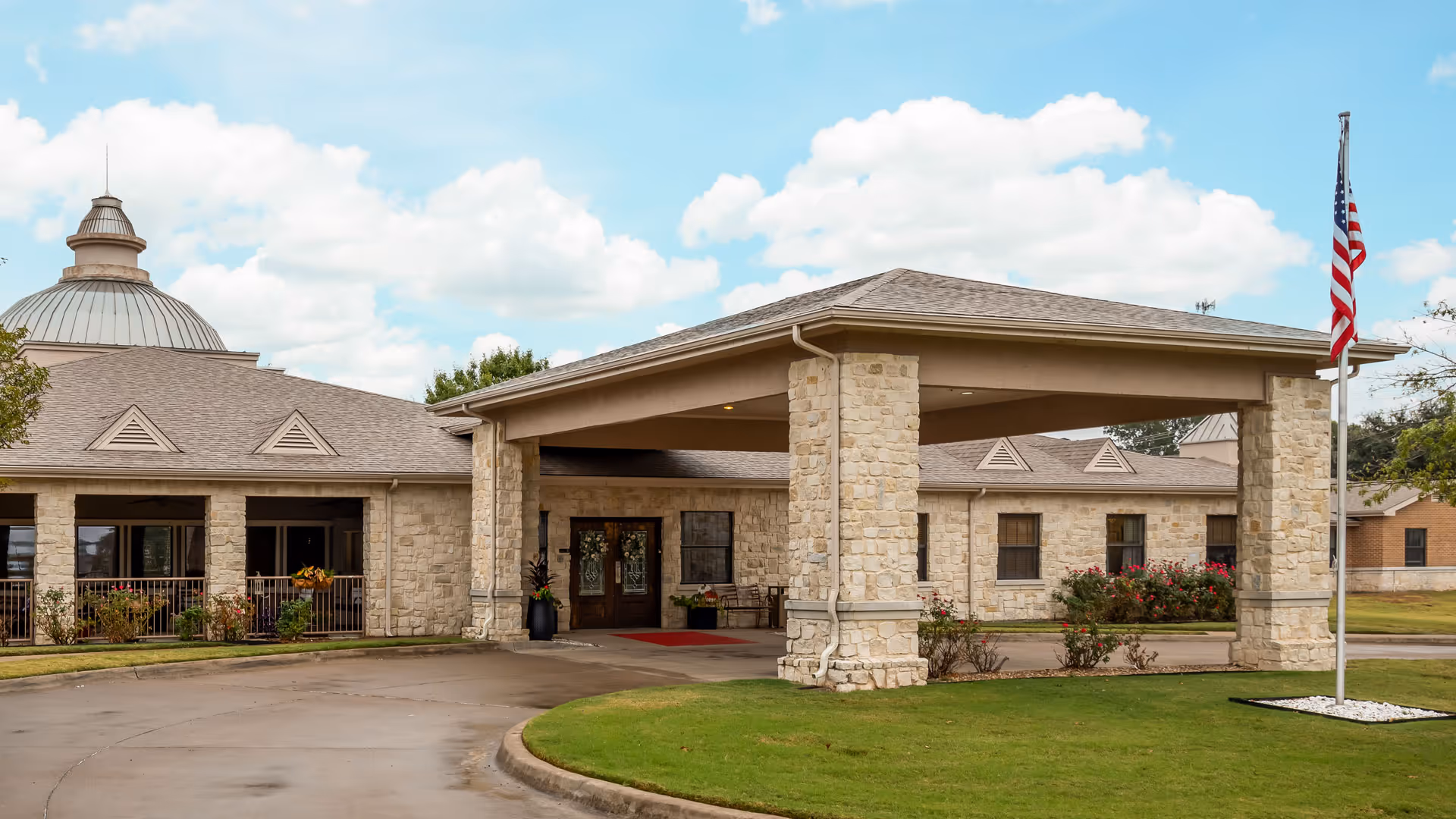 Stone-clad senior living facility entrance with a covered porte-cochère and American flag.