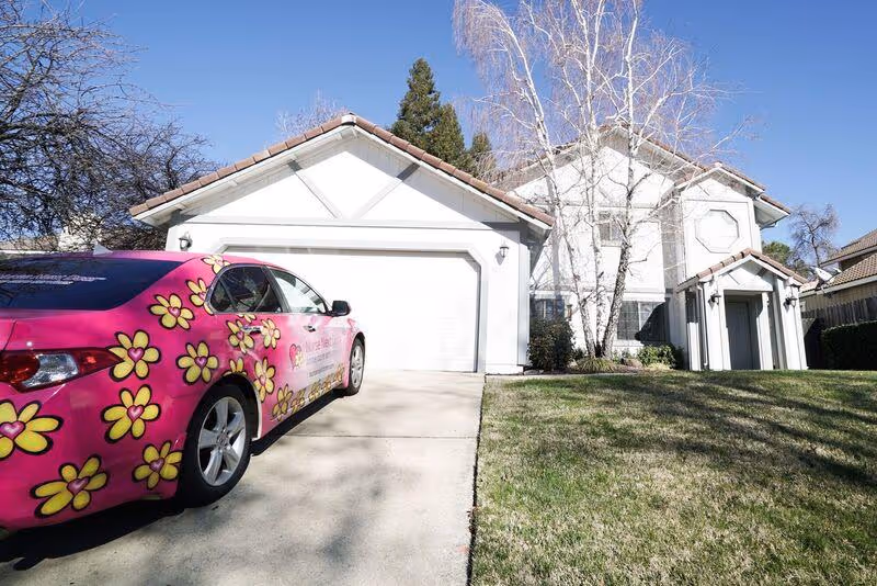 A pink car with flower decals parked in the driveway of a white two-story senior residence.