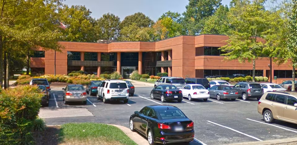 Brick building with a large parking lot and surrounding trees.