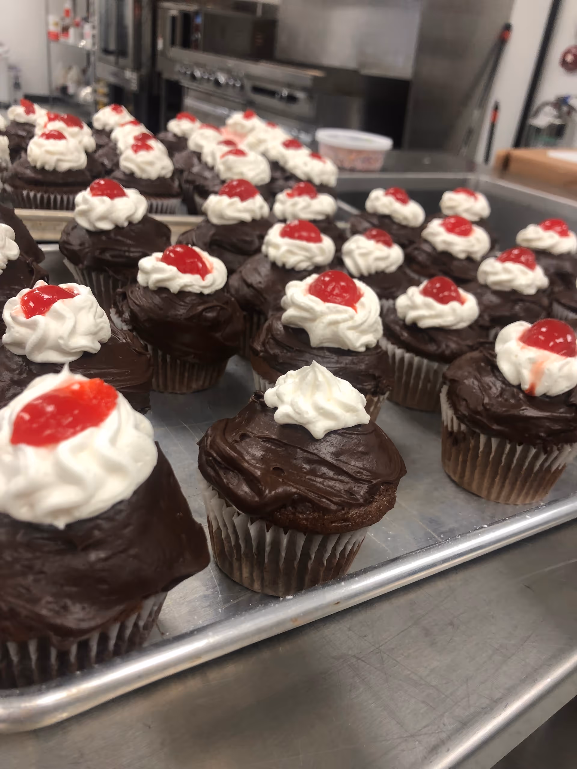 Tray of chocolate cupcakes with white frosting and red cherries in a kitchen