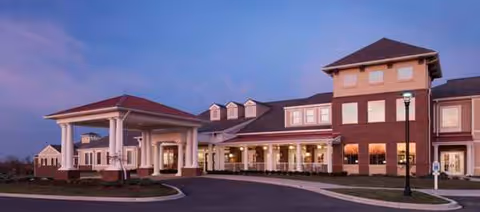 Exterior view of Valhalla Post Acute building with entrance, covered drop-off, and lamppost at dusk.