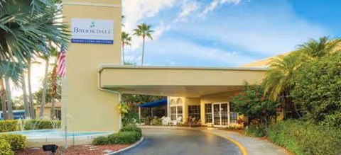 Exterior view of Brookdale Palma Sola, a senior living facility, with a driveway and palm trees.