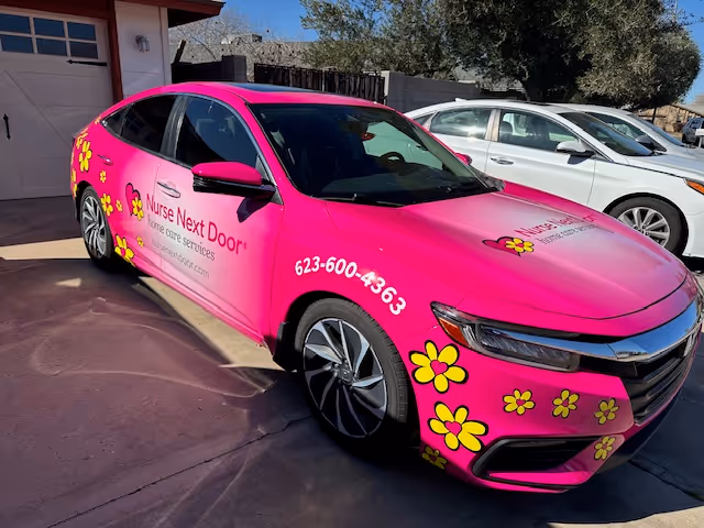 Bright pink Nurse Next Door car parked in driveway with flower decals and logo.