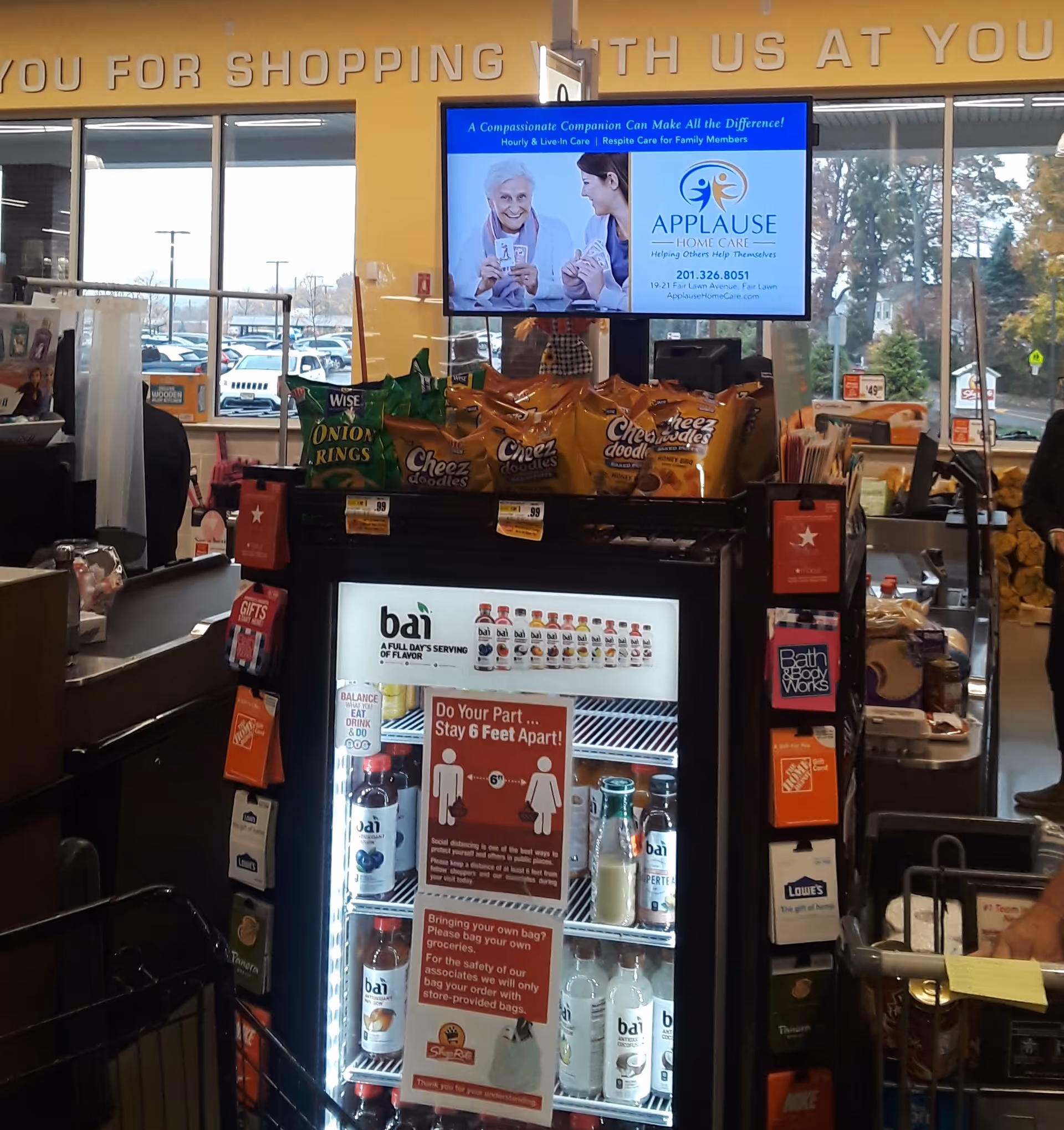 Store checkout area inside a facility featuring snack displays, beverage cooler, and Applause Home Care screen.