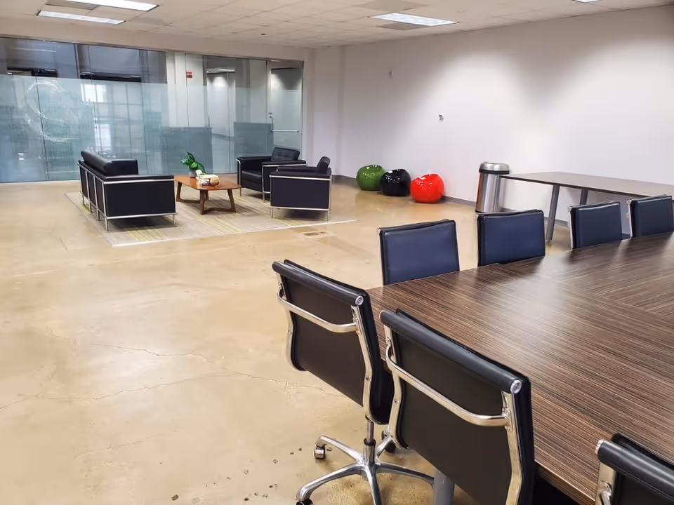 Modern interior lounge with conference table, black chairs, and glass-walled seating area.