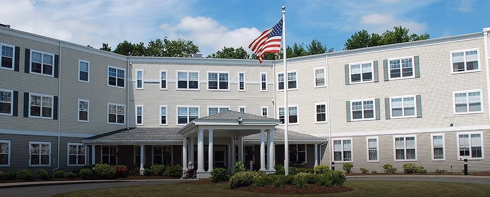 Front view of a three-story senior living facility with an American flag.