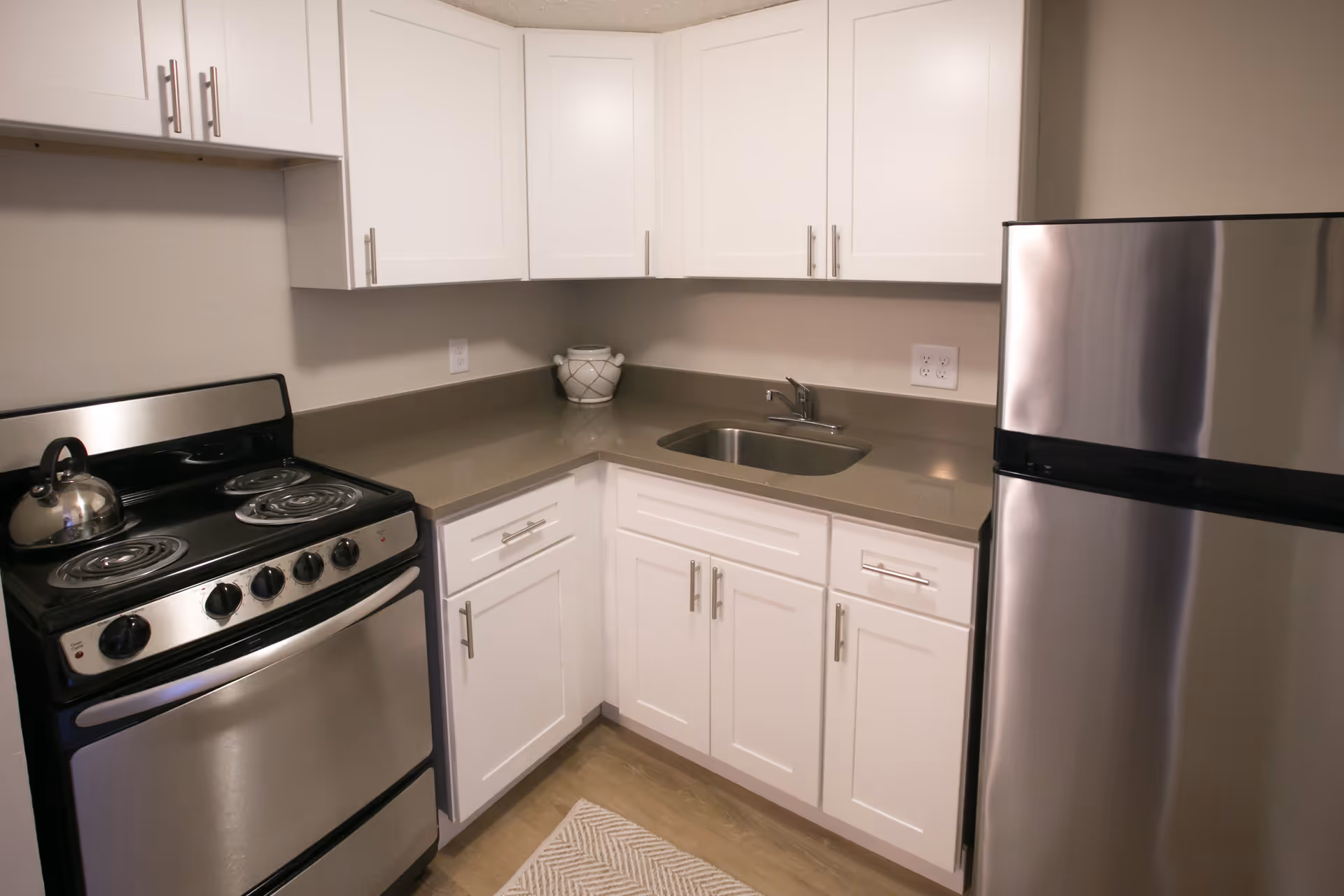 Small kitchen with white cabinets, a stainless steel stove and refrigerator, and a corner sink.
