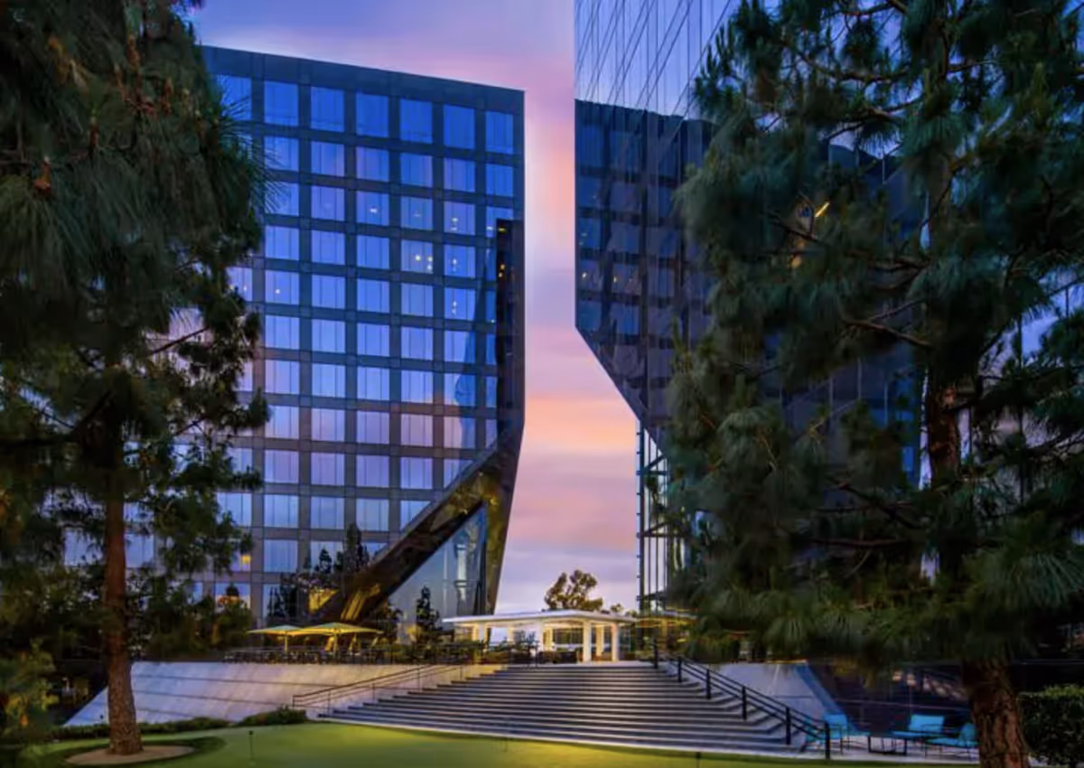 Modern glass-front building with steps, trees, and an outdoor plaza at dusk.