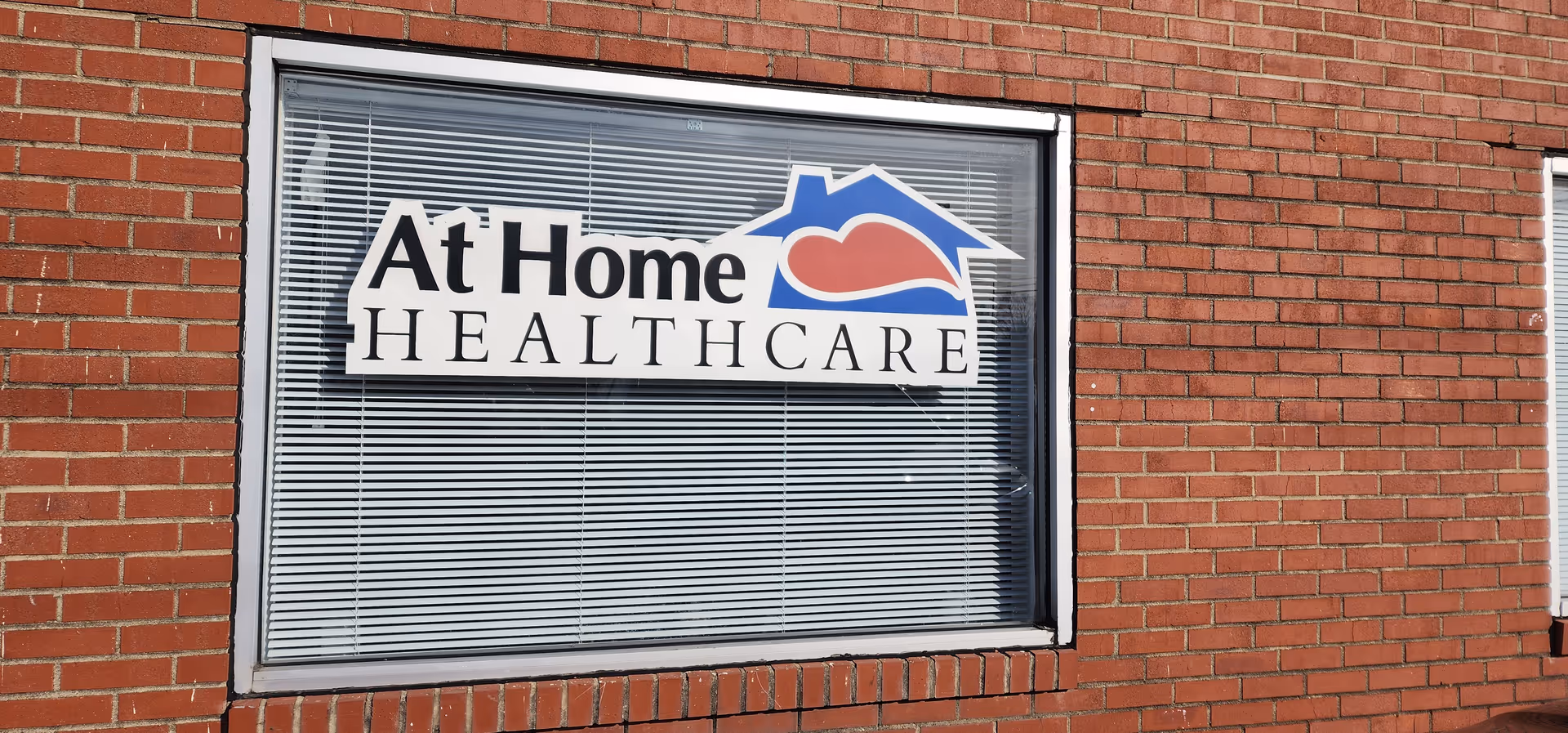 Brick exterior with a window sign reading At Home Healthcare on the building.