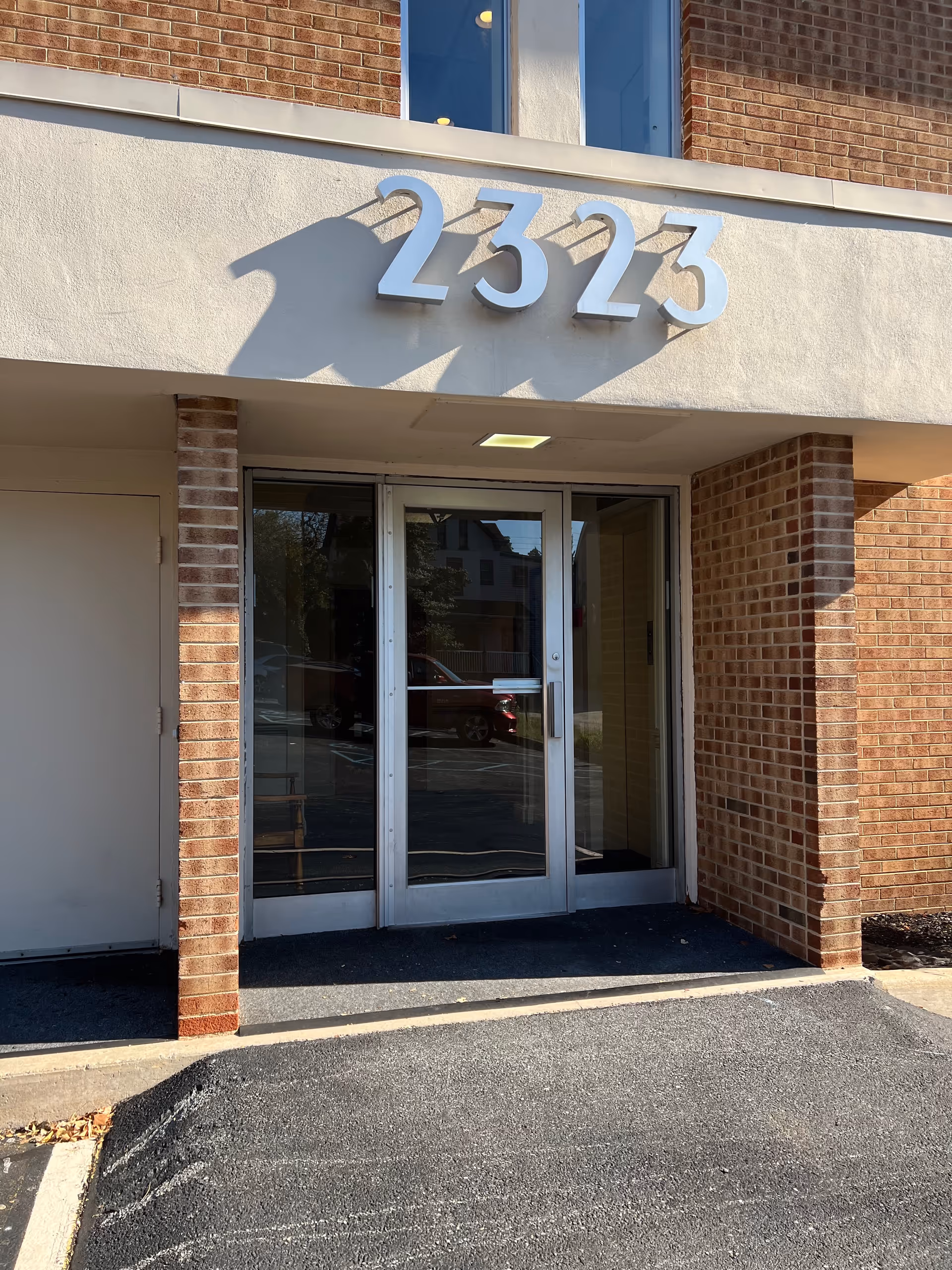 Brick exterior entrance with glass doors and the number 2323 above the doorway.