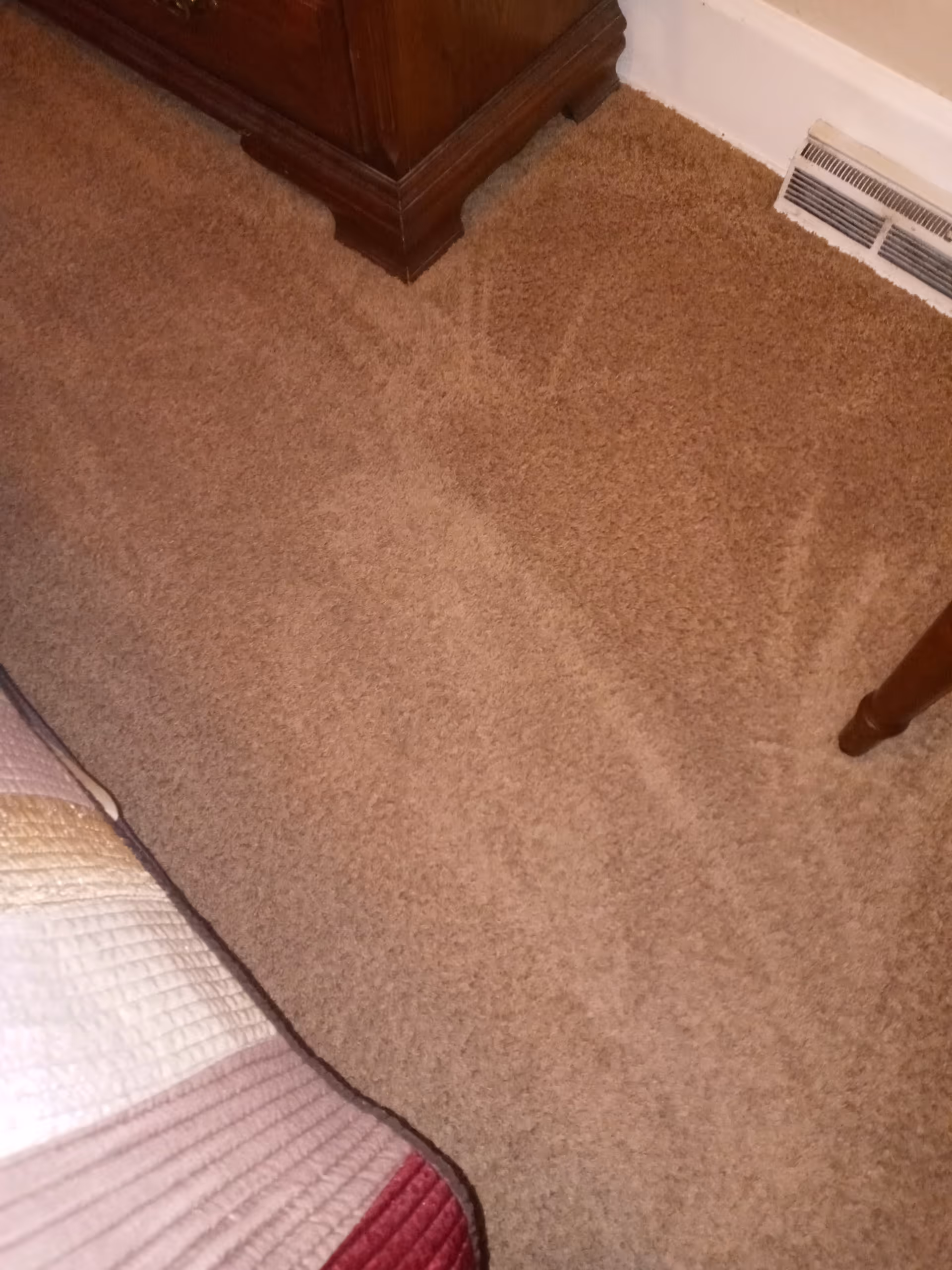 Corner of a bedroom with beige carpet, dresser, bed, and wall vent.