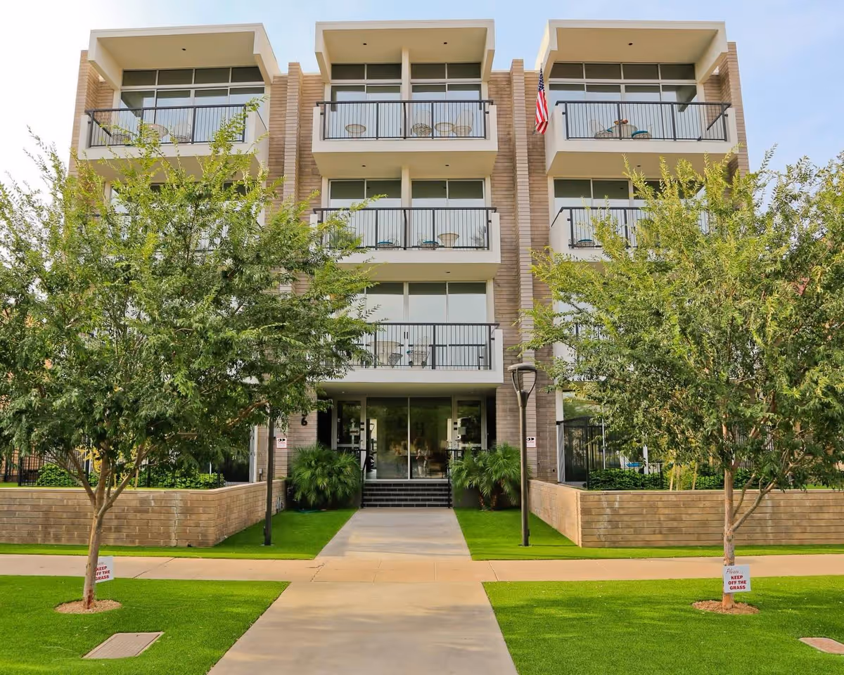 A modern four-story senior living building with balconies, glass entry, and manicured lawn