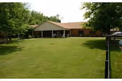 Single-story facility with a covered entrance, manicured lawn, and mature trees in front.