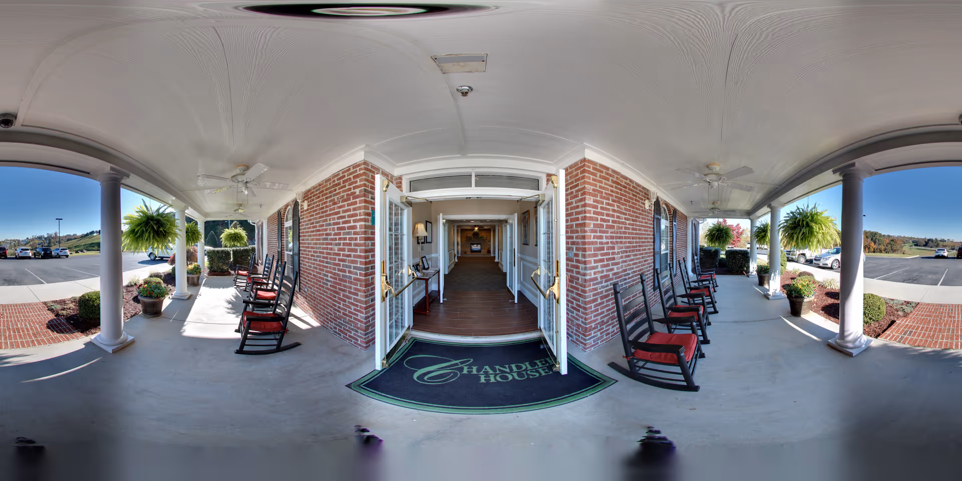 Covered front porch entrance with rocking chairs and open double doors into a senior living facility.
