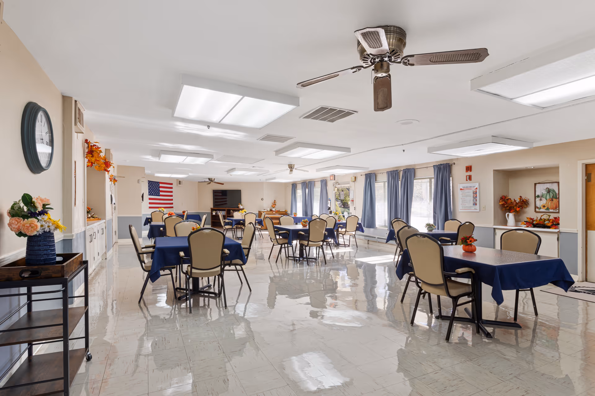 Bright dining room in a senior living facility with blue tablecloths and many tables.