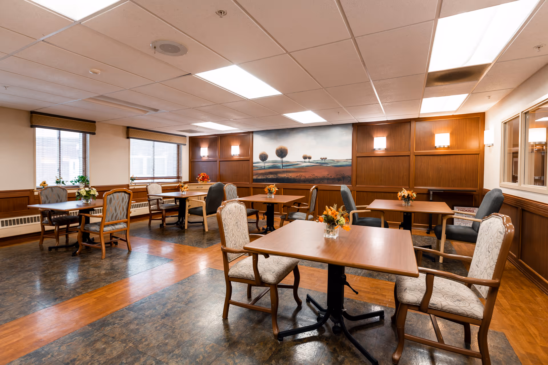 Facility dining room with wood tables, chairs, and wall artwork.