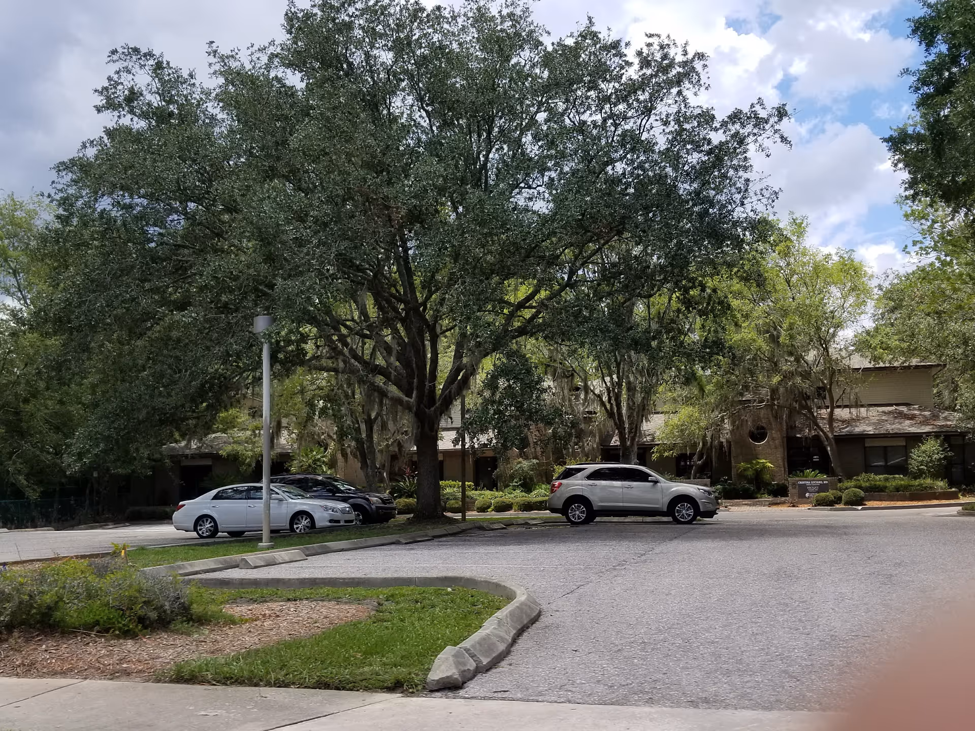 Parking lot in front of Brooks Rehabilitation Home Health building with large shade trees.