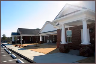Brick senior living facility exterior with white-columned entrance and paved front walkway.