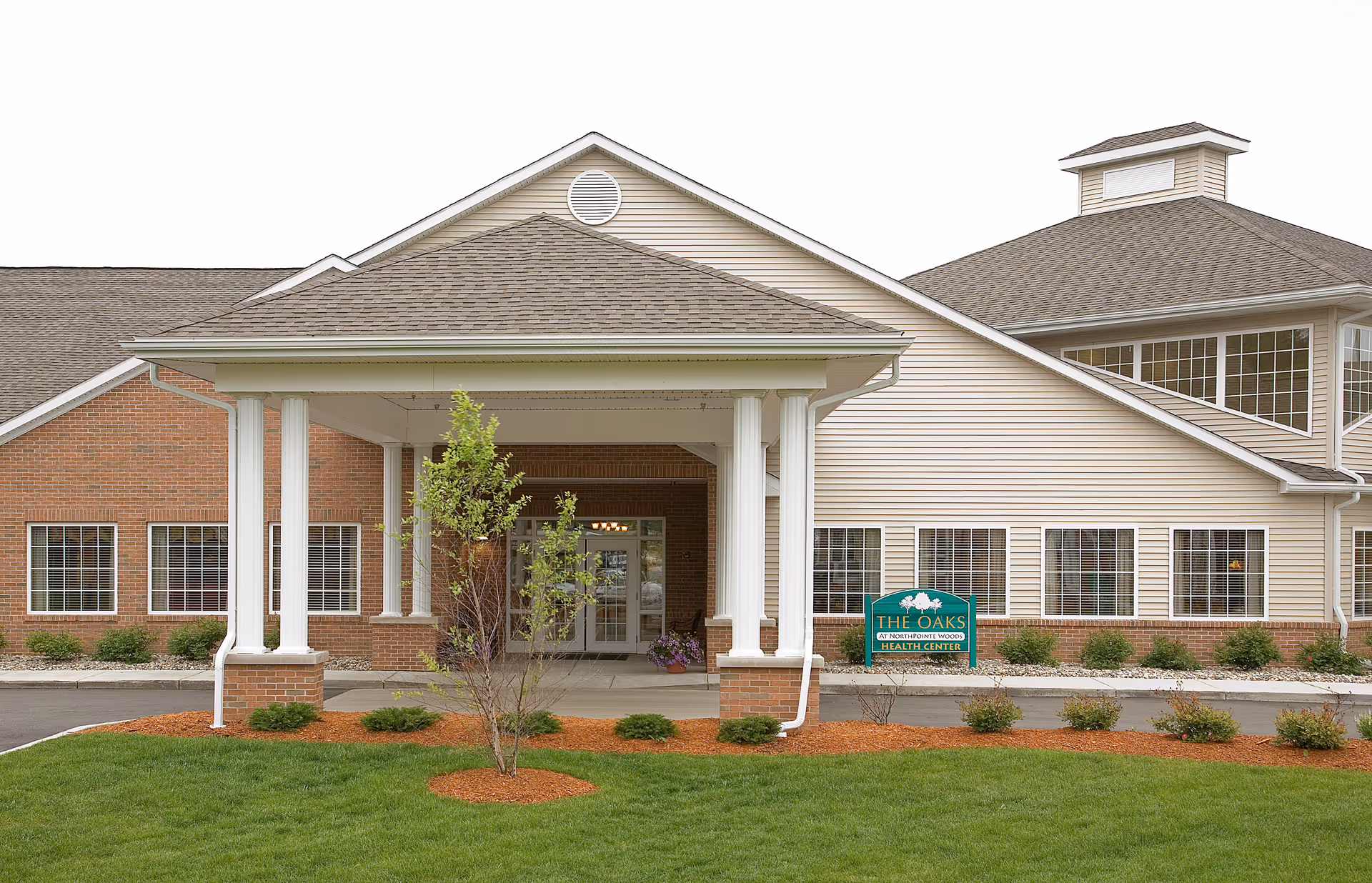 Exterior view of The Oaks at North Pointe Woods entrance with covered walkway and sign.