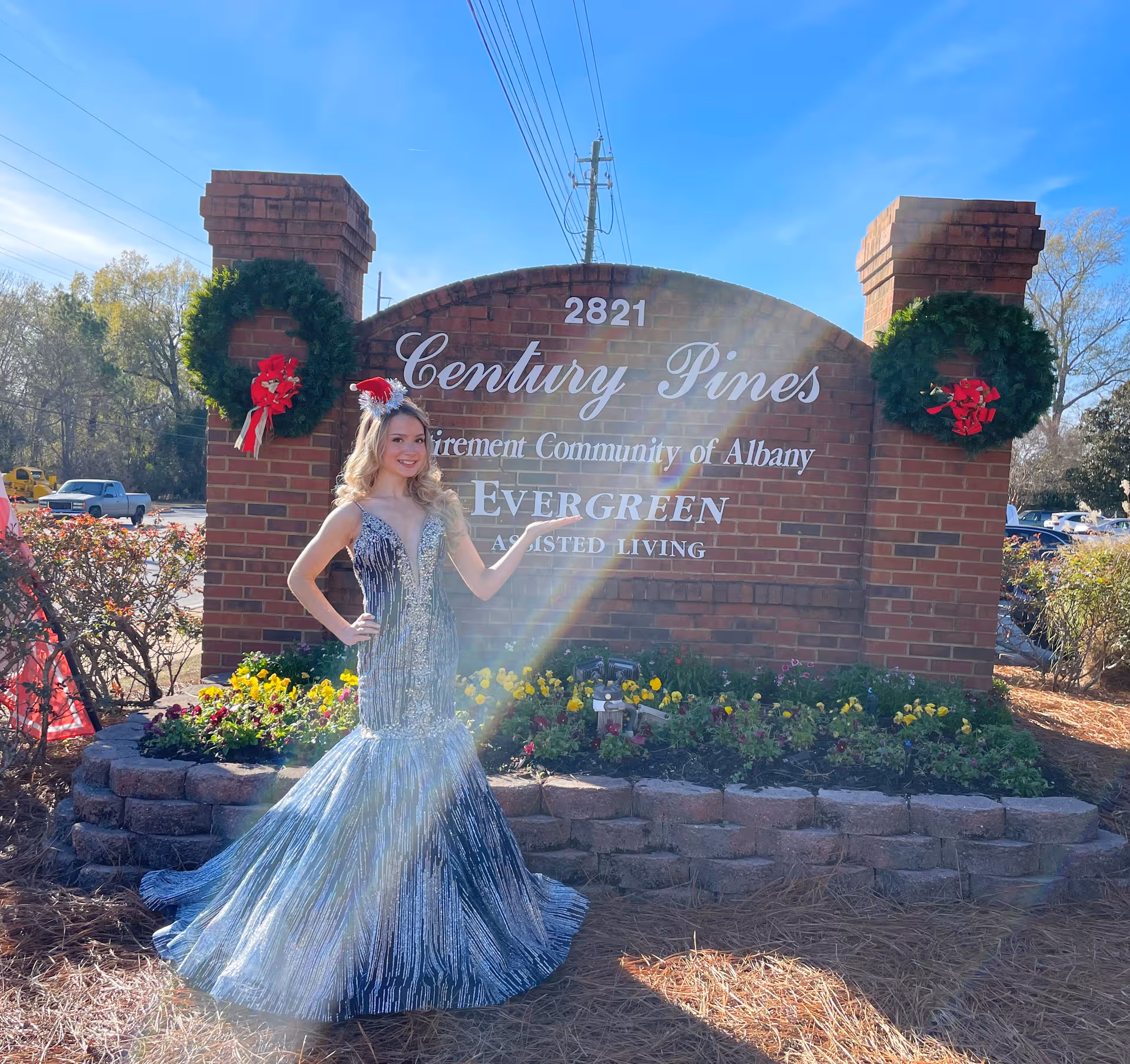 A woman in a sparkling gown poses beside the Century Pines front entrance sign.
