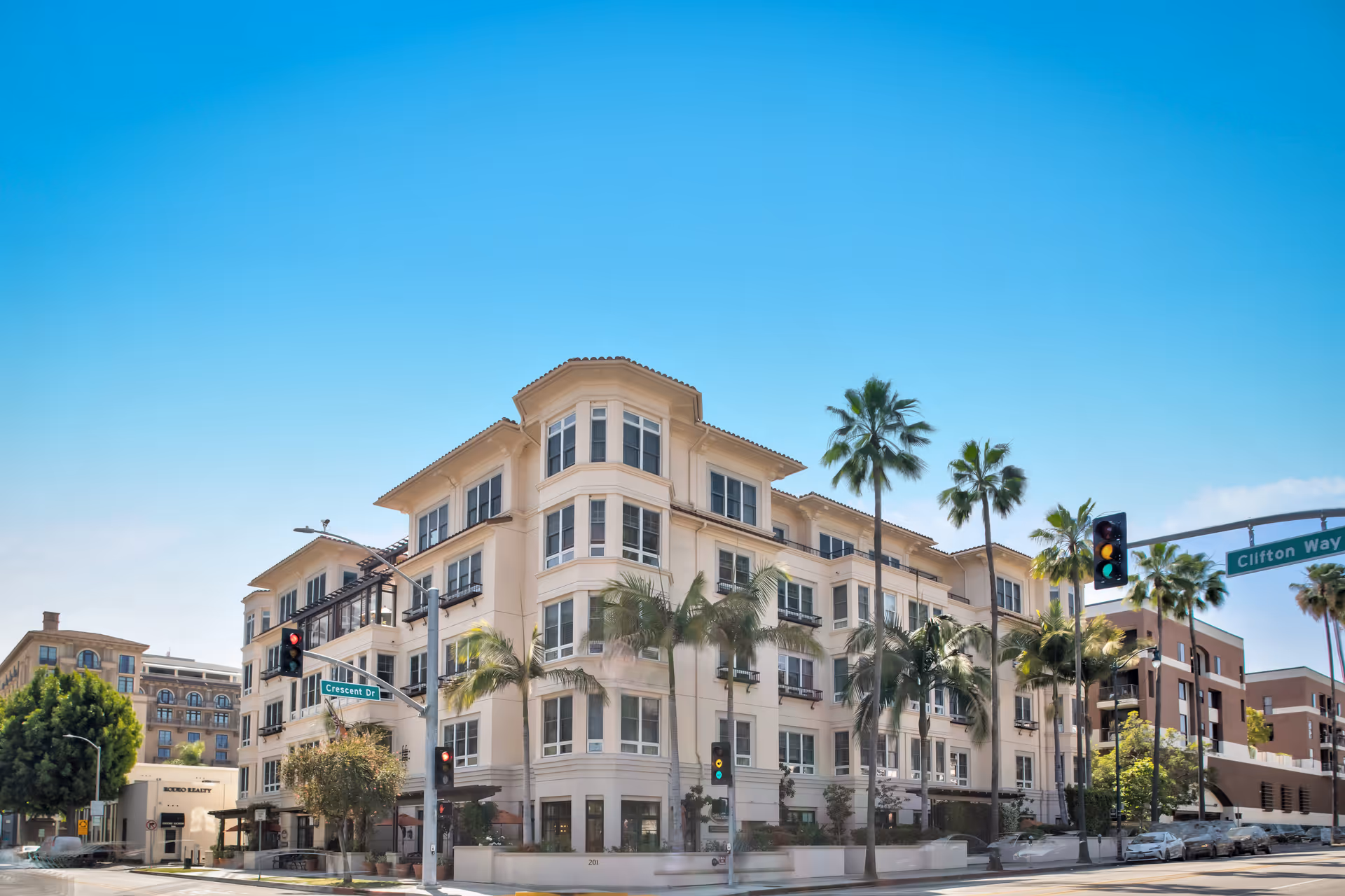Sunrise of Beverly Hills building exterior on sunny street corner with palm trees.