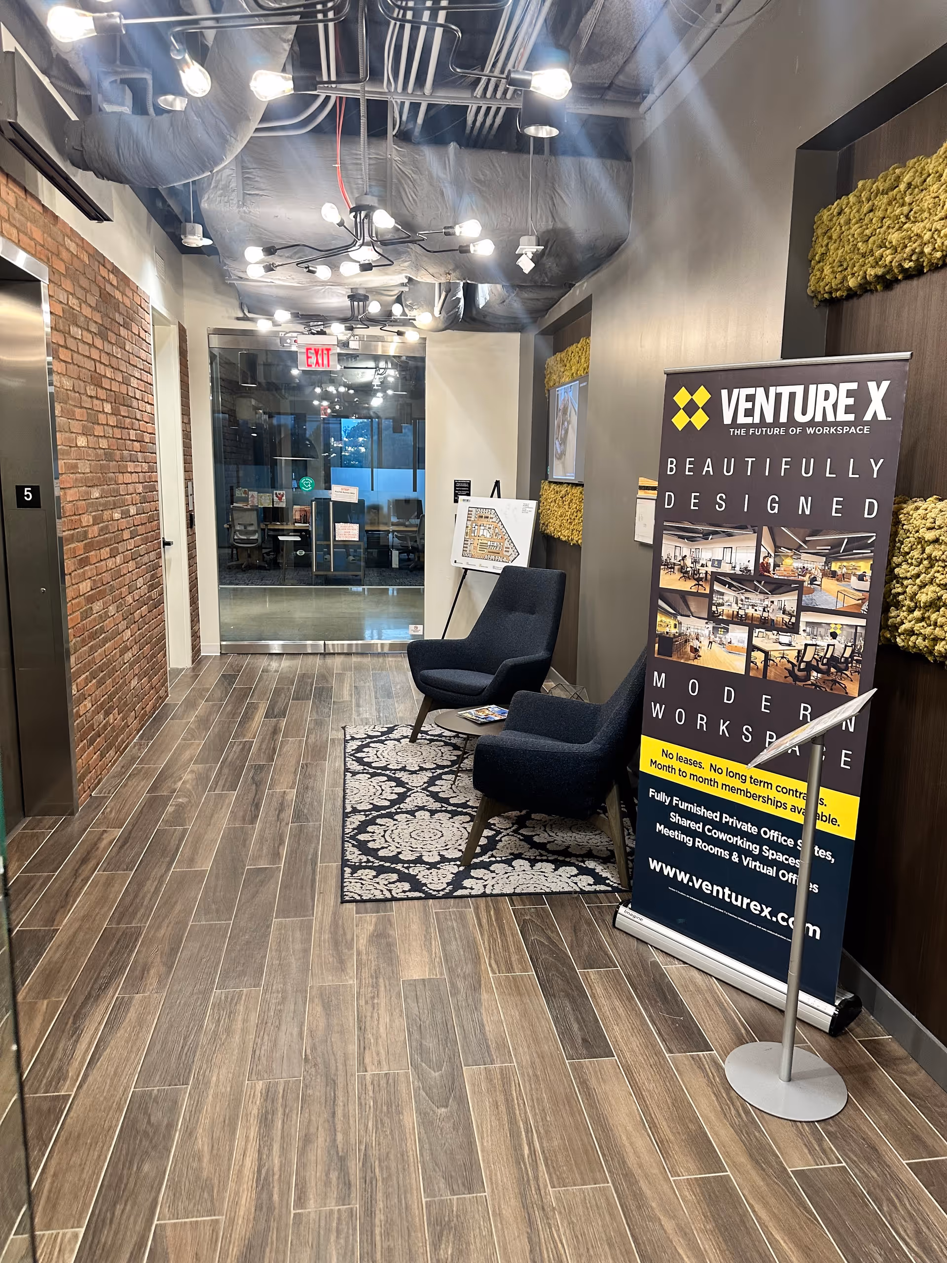 Modern indoor lobby with exposed ceiling, seating, rug, and a promotional banner.