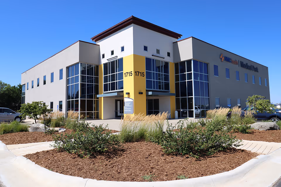 Modern senior living facility exterior with glass windows and yellow entrance column.