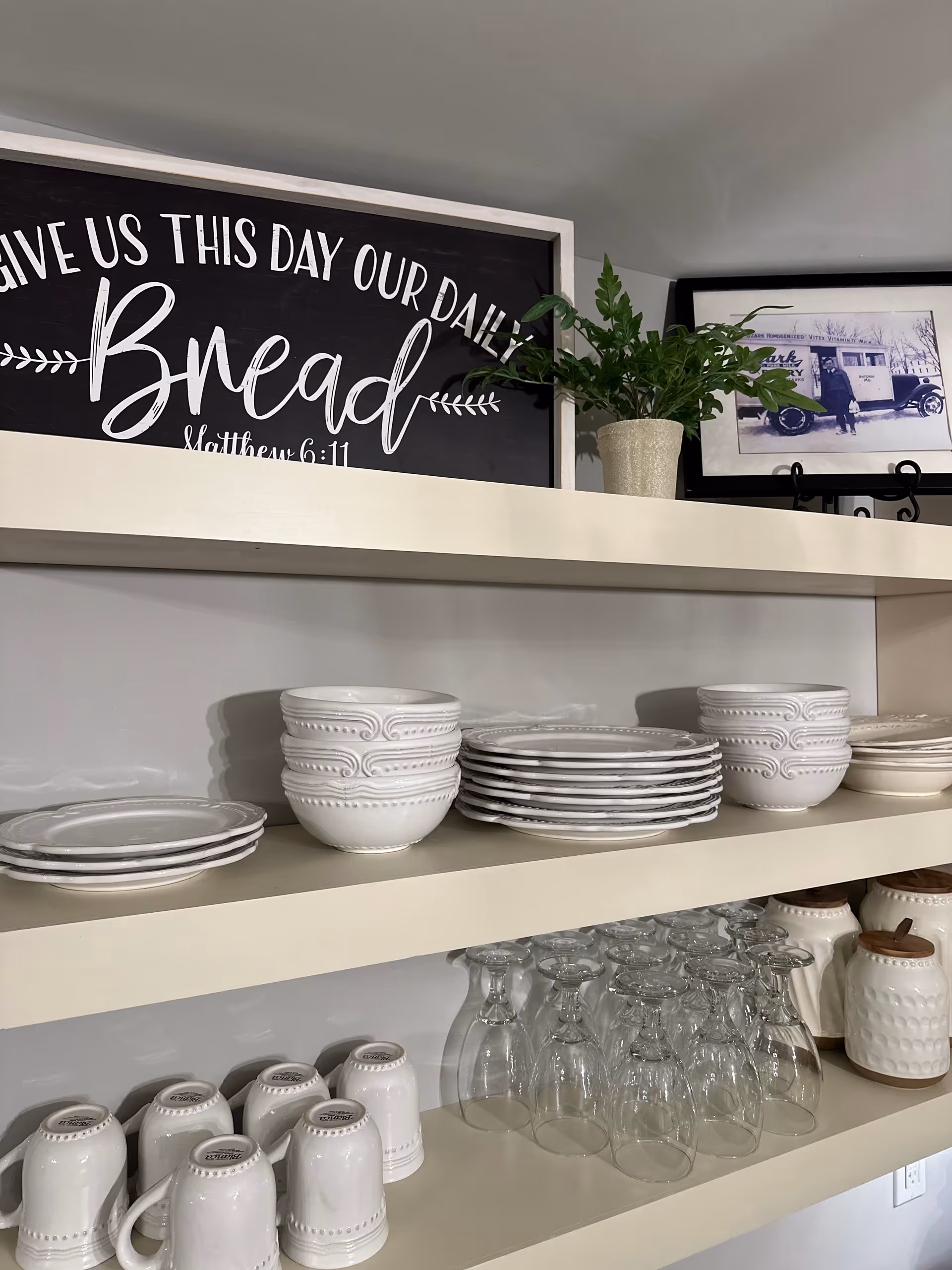 Shelves hold white dishes, bowls, mugs, and glassware with a bread-themed sign above.