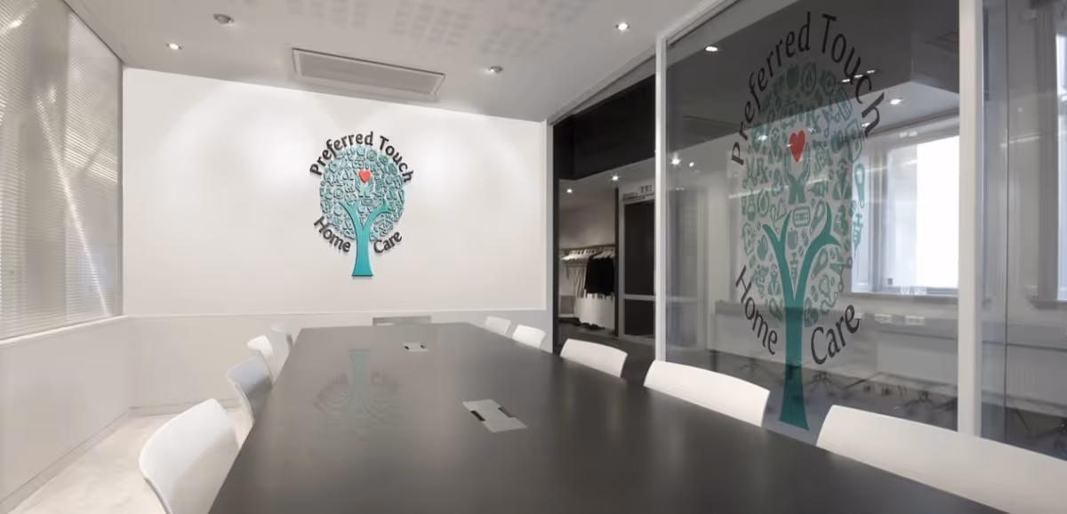 Modern conference room with a long black table, white chairs, and glass walls displaying a logo.