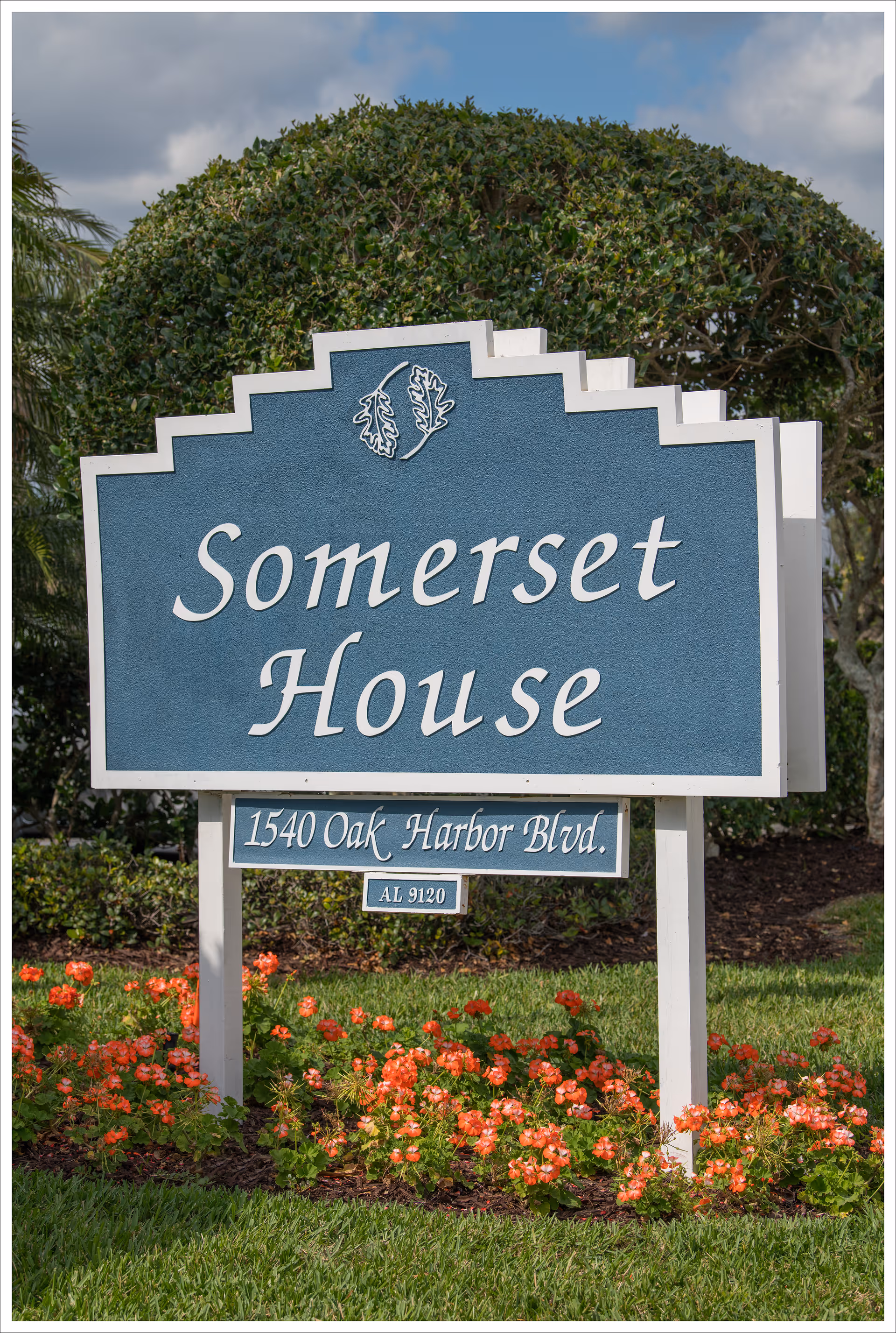 Blue Somerset House entrance sign with the address 1540 Oak Harbor Blvd surrounded by flowers and landscaping.