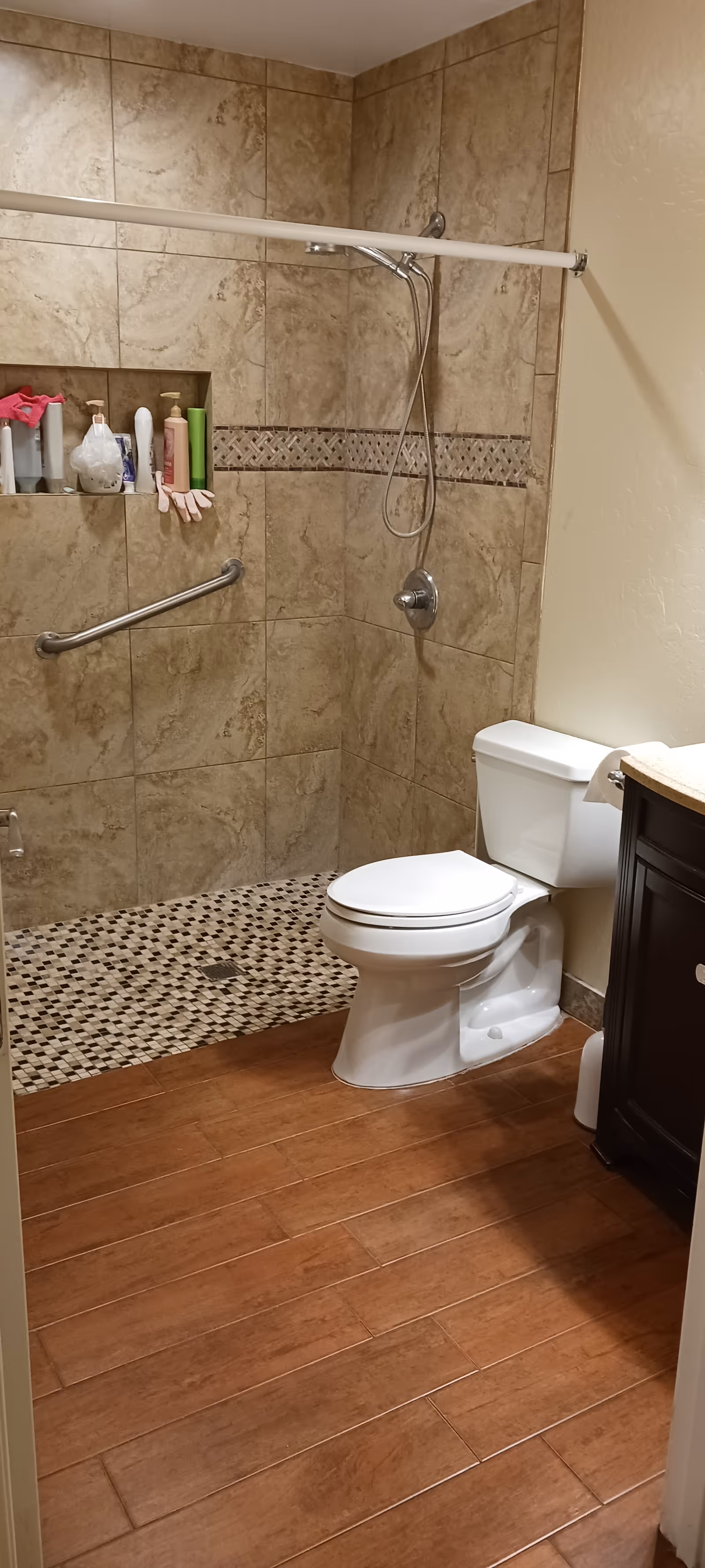 Accessible tiled bathroom with a shower, grab bars, toilet, and vanity.