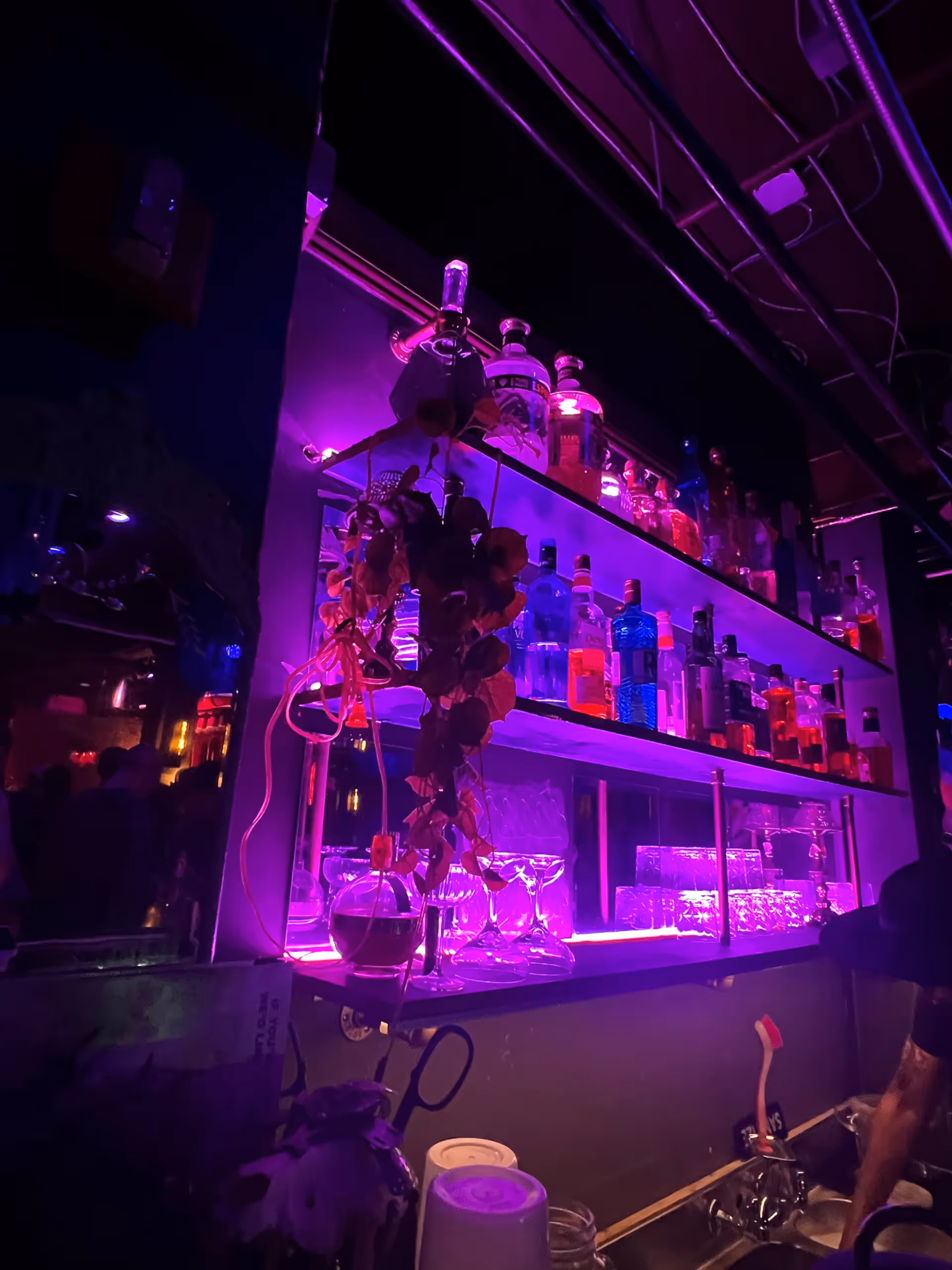 A dimly lit bar area with purple lighting, illuminated shelves, and bottles.