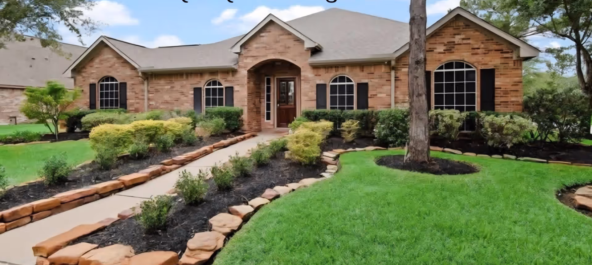 A brick senior living facility front with arched windows, landscaping, and a stone walkway.