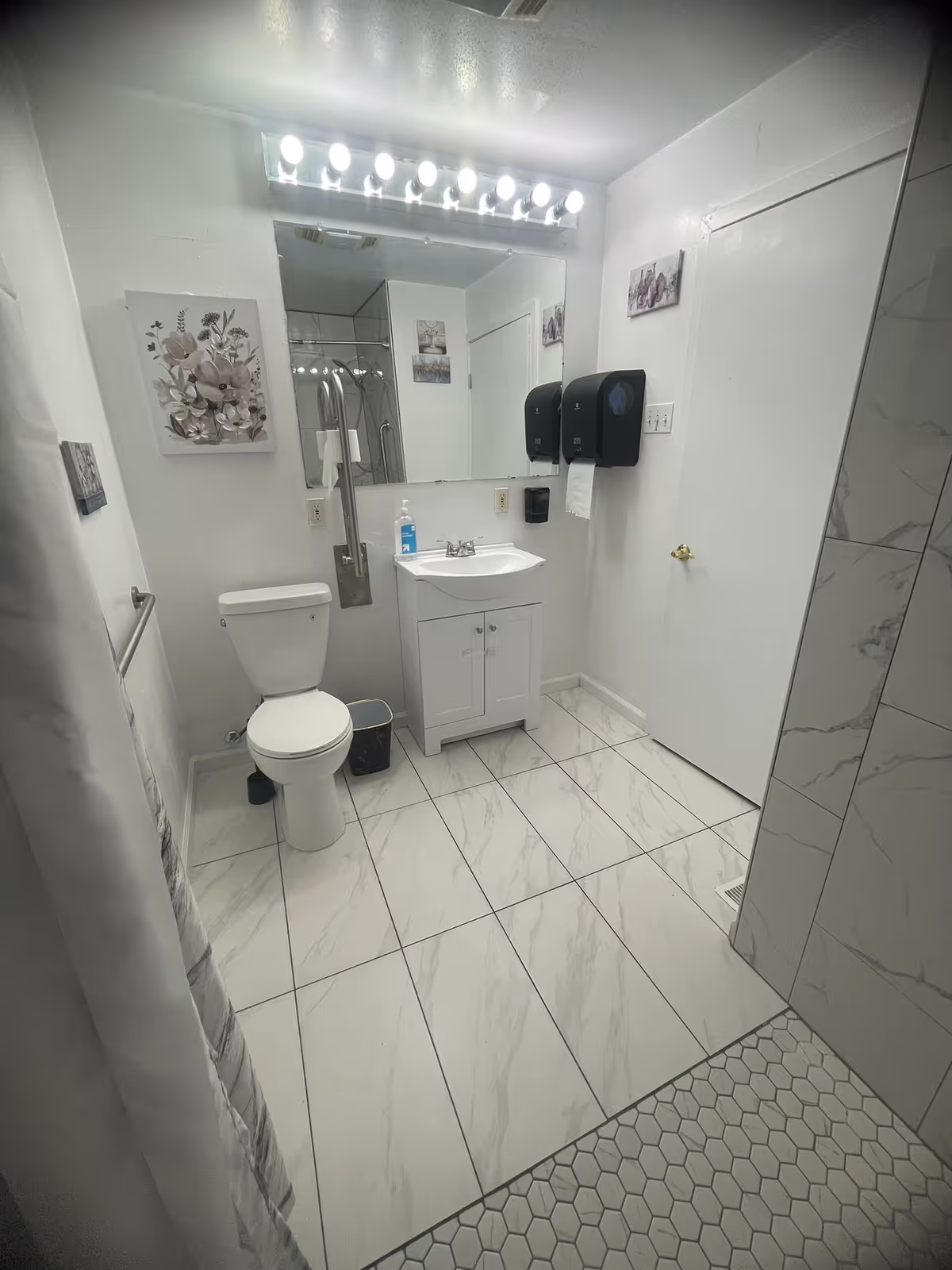 White-tiled bathroom with toilet, sink, mirror, and shower in a care facility.